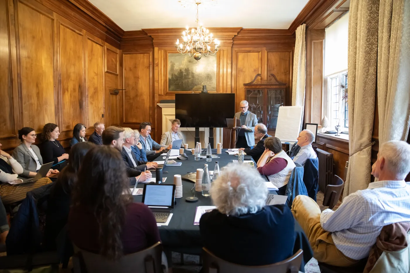 Academics seated around a long table in a wood-panelled room at Yarnton Manor as a speaker presents.
