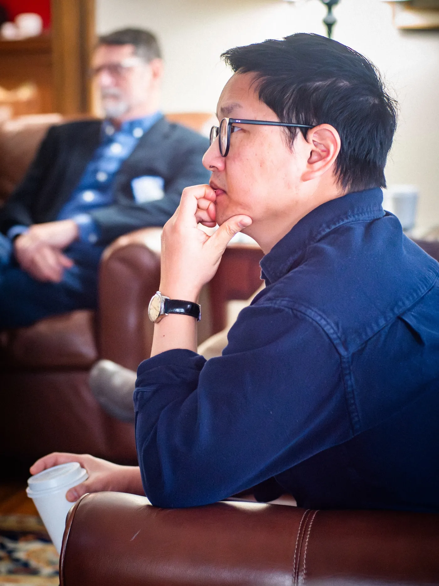 A scholar listening thoughtfully during a retreat session with coffee in hand.